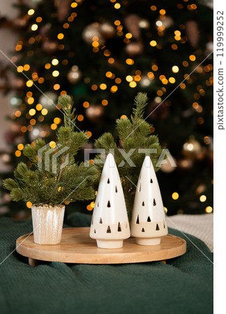 Festive holiday decor with miniature Christmas trees and ceramic ornaments on a wooden tray, cozy and warm ambiance. 119999252
