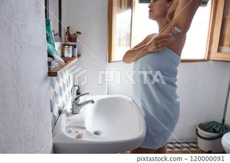 Woman in towel shaving armpits in bright bathroom setting 120000091