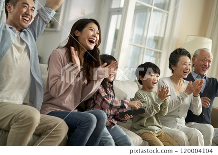 happy three generation asian family sitting on couch watching sport game on tv 120004104