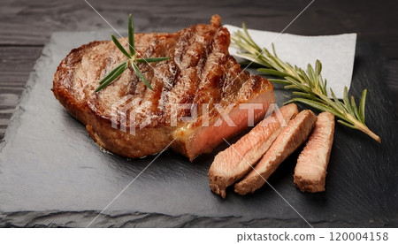Medium rare juicy steak, parchment paper and rosemary on a slate plate Medium rare juicy steak, parchment paper and rosemary on a slate plate 120004158