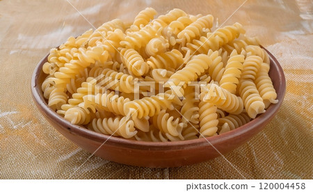 A bowl of raw rotini pasta, a type of pasta that is shaped like a spiral or a bottle of wine 120004458