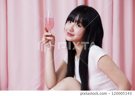 A Korean woman in her 20s holding a champagne glass with a pink drink on a pink background 120005143