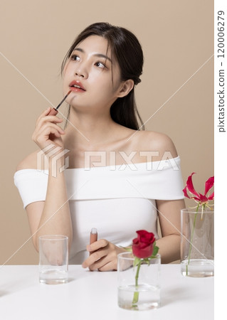 a woman in her 20s holding cosmetics in front of a table decorated with flowers 120006279