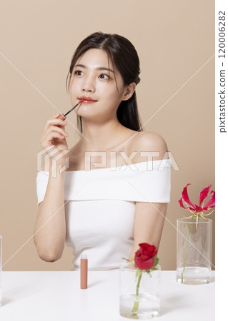 a woman in her 20s holding cosmetics in front of a table decorated with flowers 120006282
