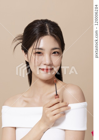a woman in her 20s holding cosmetics in front of a table decorated with flowers 120006284