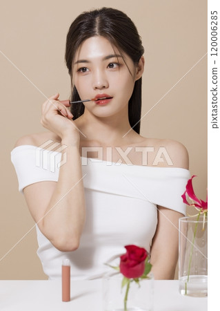 a woman in her 20s holding cosmetics in front of a table decorated with flowers 120006285