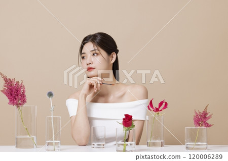 a woman in her 20s holding cosmetics in front of a table decorated with flowers a woman in her 20s holding cosmetics in front of a table decorated with flowers 120006289