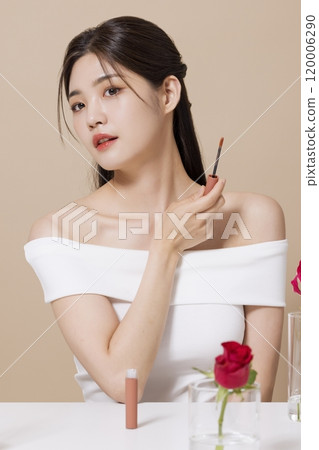 a woman in her 20s holding cosmetics in front of a table decorated with flowers 120006290