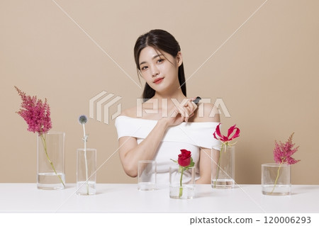 a woman in her 20s holding cosmetics in front of a table decorated with flowers 120006293