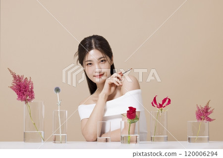 a woman in her 20s holding cosmetics in front of a table decorated with flowers 120006294