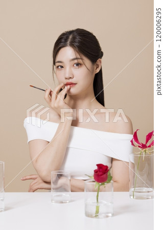a woman in her 20s holding cosmetics in front of a table decorated with flowers 120006295