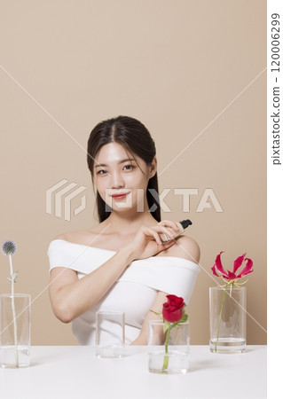 a woman in her 20s holding cosmetics in front of a table decorated with flowers 120006299