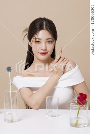 a woman in her 20s holding cosmetics in front of a table decorated with flowers 120006303