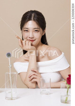 a woman in her 20s holding cosmetics in front of a table decorated with flowers a woman in her 20s holding cosmetics in front of a table decorated with flowers 120006304