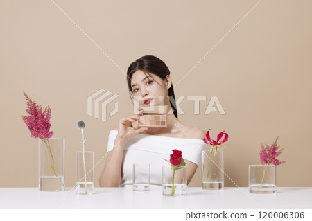 a woman in her 20s holding cosmetics in front of a table decorated with flowers a woman in her 20s holding cosmetics in front of a table decorated with flowers 120006306
