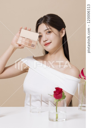 a woman in her 20s holding cosmetics in front of a table decorated with flowers a woman in her 20s holding cosmetics in front of a table decorated with flowers 120006313