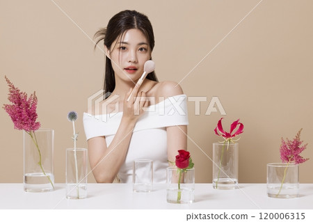 a woman in her 20s holding cosmetics in front of a table decorated with flowers 120006315