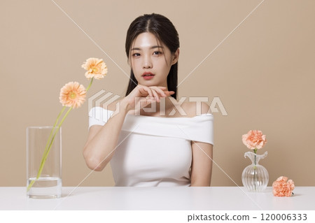 a woman in her 20s holding cosmetics in front of a table decorated with flowers 120006333