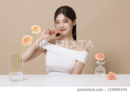 a woman in her 20s holding cosmetics in front of a table decorated with flowers 120006334