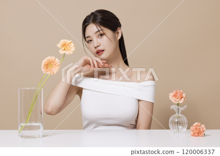 a woman in her 20s holding cosmetics in front of a table decorated with flowers a woman in her 20s holding cosmetics in front of a table decorated with flowers 120006337