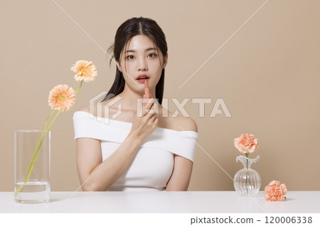 a woman in her 20s holding cosmetics in front of a table decorated with flowers 120006338