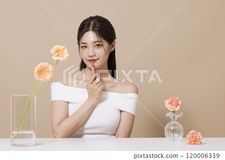 a woman in her 20s holding cosmetics in front of a table decorated with flowers 120006339