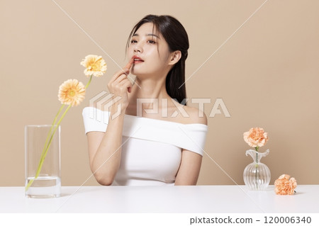 a woman in her 20s holding cosmetics in front of a table decorated with flowers 120006340