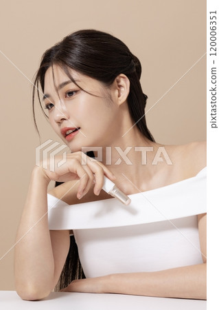 a woman in her 20s holding cosmetics in front of a table decorated with flowers 120006351