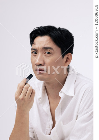 A pose of a middleaged man applying lip balm to his lips A pose of a middleaged man applying lip balm to his lips 120006919
