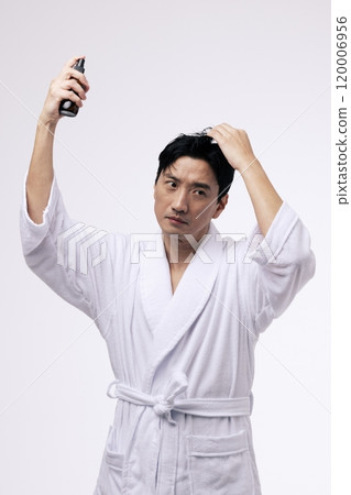 A middleaged man holding a spray bottle and spraying mist on his head 120006956
