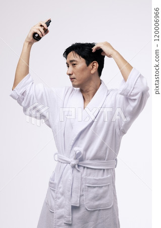A middleaged man holding a spray bottle and spraying mist on his head 120006966