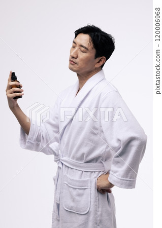 Middleaged man holding a spray bottle and spraying mist on his face Middleaged man holding a spray bottle and spraying mist on his face 120006968