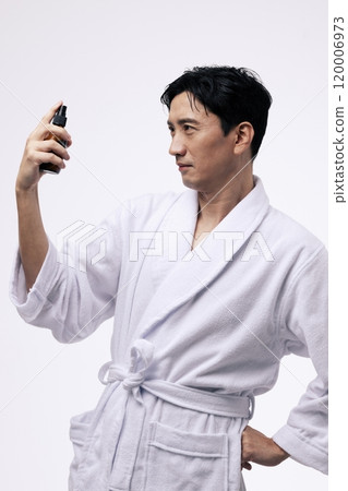Middleaged man holding a spray bottle and spraying mist on his face 120006973
