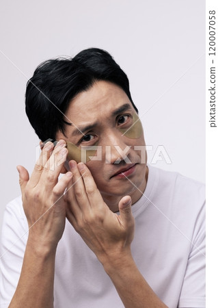 A middleaged man attaching an eye patch to his eye area with his finger. 120007058