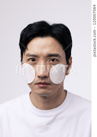 Closeup of a middleaged man with round cotton pads attached to both cheeks 120007064