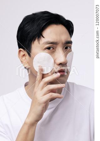 A middleaged man applying a round cotton pad 120007073