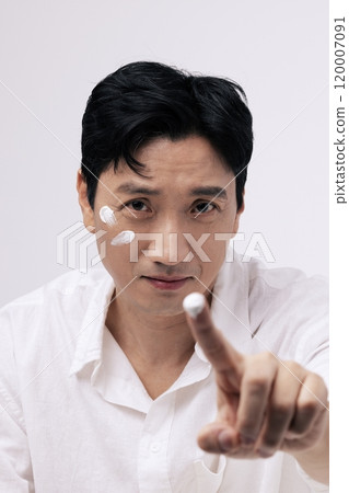 Middleaged man applying cream with his fingers and looking straight ahead 120007091