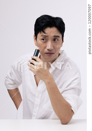 A middleaged man wearing a white shirt and applying foundation to his face A middleaged man wearing a white shirt and applying foundation to his face 120007097