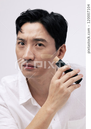 A middleaged man applying foundation to his face with an expressionless expression A middleaged man applying foundation to his face with an expressionless expression 120007104