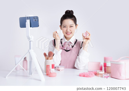 A teenage woman in school uniform laying out various cosmetics and filming a video with her smartphone 120007743
