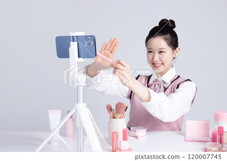 A teenage woman in school uniform laying out various cosmetics and filming a video with her smartphone A teenage woman in school uniform laying out various cosmetics and filming a video with her smartphone 120007745