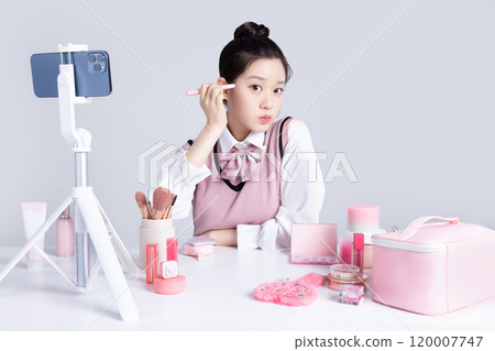 A teenage woman in school uniform laying out various cosmetics and filming a video with her smartphone 120007747