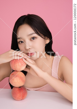 A woman in her 20s posing with a peach on the table 120008172