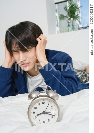 A man in his 20s suffering from the sound of an alarm clock A man in his 20s suffering from the sound of an alarm clock 120008317