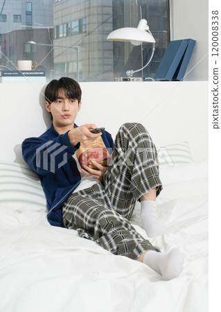 A man in his 20s operating a remote control while lying in bed A man in his 20s operating a remote control while lying in bed 120008338