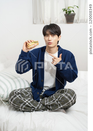 A man in his 20s sitting on the bed and eating bread 120008349