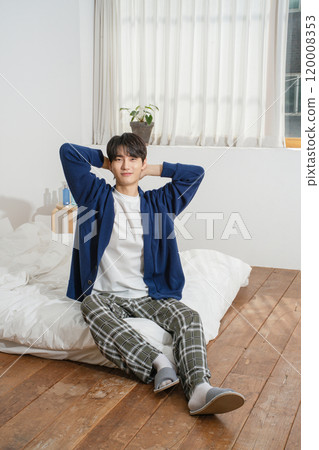 A man in his 20s sitting on a bed in comfortable clothes 120008353