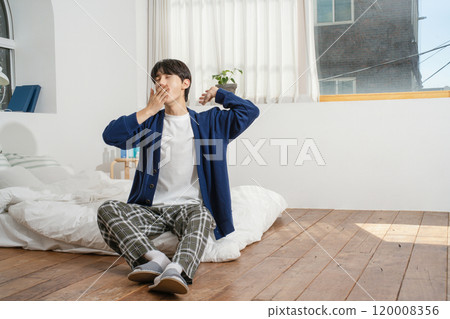 A man in his 20s sitting on a bed in comfortable clothes 120008356