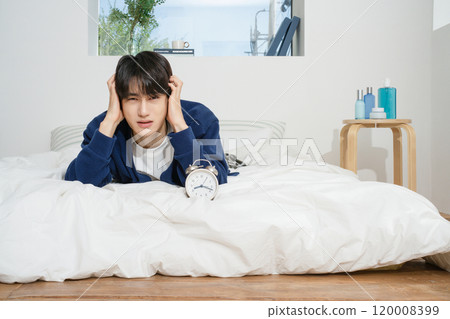 A man in his 20s suffering from the sound of an alarm clock A man in his 20s suffering from the sound of an alarm clock 120008399