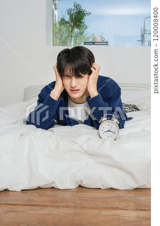A man in his 20s suffering from the sound of an alarm clock 120008400